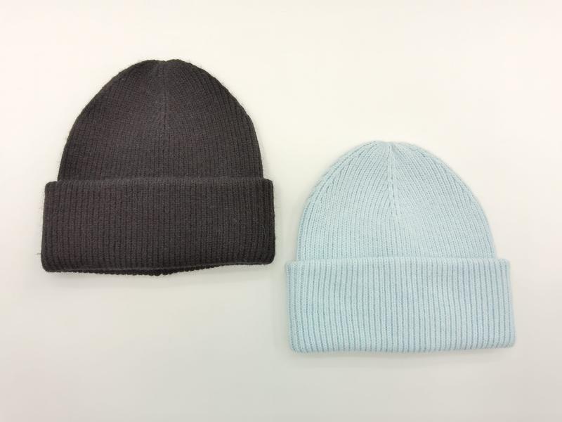 Dwie czapki beanie w prążkowany splot z mankietem: antracytowa i jasnoniebieska, ułożone płasko na białym tle.