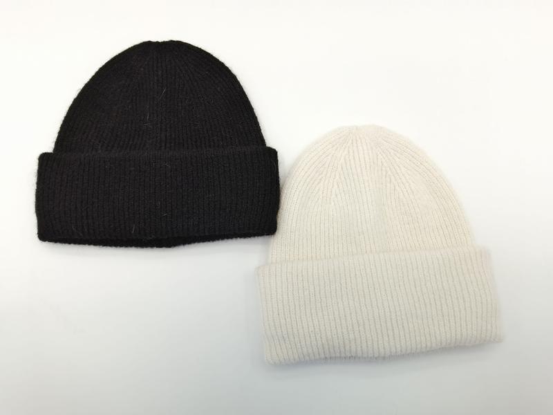 Dwie czapki beanie z prążkowanej dzianiny z mankietem, czarna i kremowa, ułożone płasko — miękkie czapki zimowe.