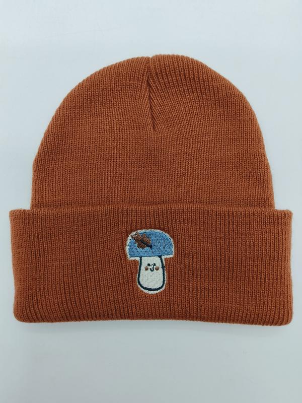 Rdzawopomarańczowa prążkowana czapka beanie z zawiniętym mankietem i niebiesko-białą haftowaną naszywką grzyba.