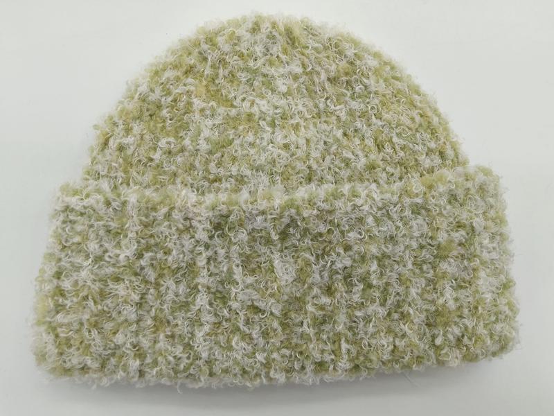 Szałwiowo-zielona czapka beanie z kremowym bouclé, podwiniętym mankietem i kręconą teksturą, na białym tle.