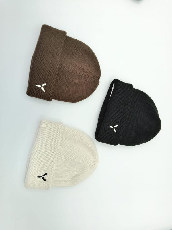 Trzy złożone czapki beanie w kolorach brązowym, czarnym i kremowym z małym haftowanym logo na białym tle.