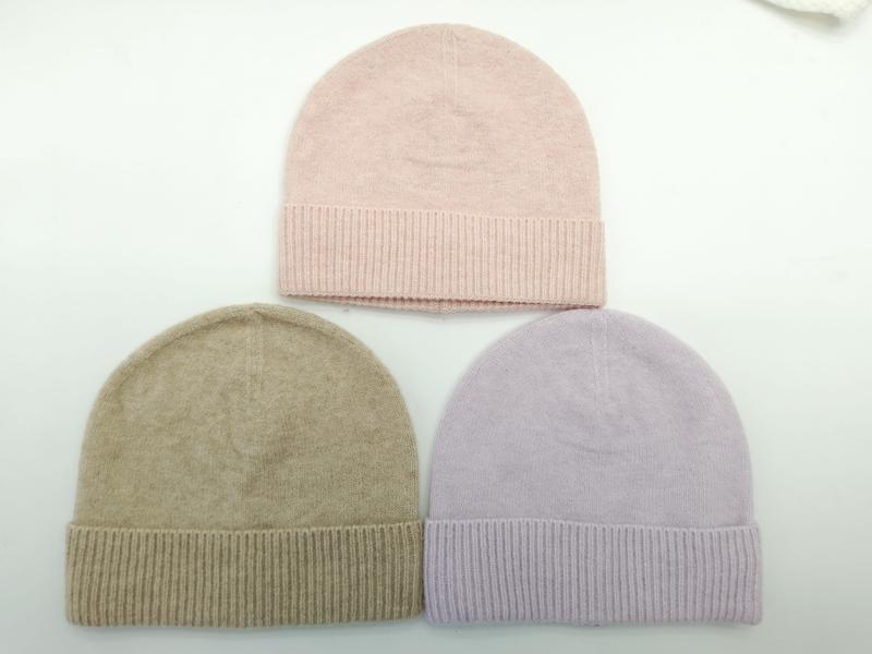 Trzy czapki beanie z dzianiny w kolorach pudrowego różu, taupe i lawendy z prążkowanymi mankietami na białym tle.