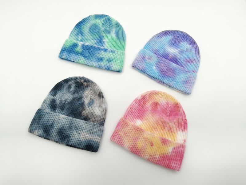 Cztery czapki beanie tie-dye w kolorach niebiesko-zielonym, fioletowo-niebieskim, ciemnoszarym i różowo-żółtym na białym tle.